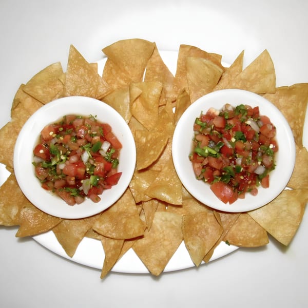 Two white bowls of fresh salsa surrounded by crispy tortilla chips on a white platter.