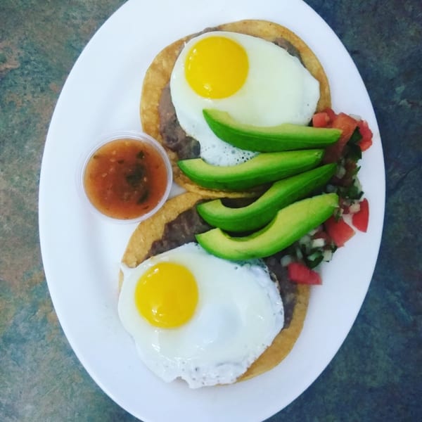 Two fried eggs on tortillas with refried beans, avocado slices, pico de gallo, and salsa.