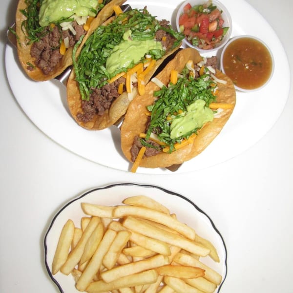 Three beef tacos with guacamole, lettuce, and cheese, served with salsa, pico de gallo, and fries.