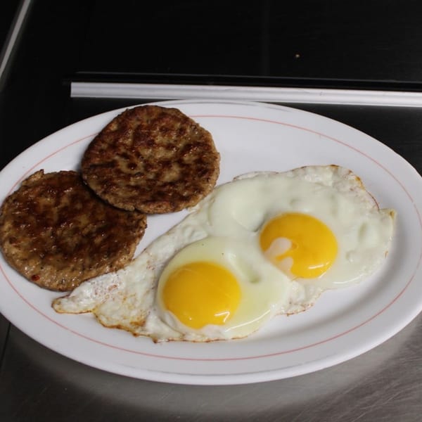 Two fried eggs with bright yellow yolks and two sausage patties on a white plate.